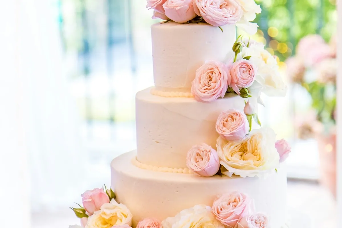 Mehrstoeckige weisse Hochzeitstorte mit rosa Rosen und Blumendekor